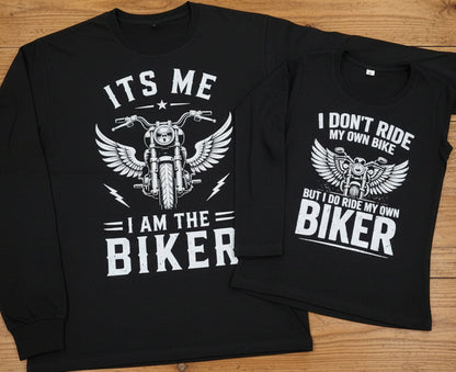 Two black graphic t-shirts laid flat on a wooden surface, showing matching biker-themed designs with white text and a winged motorcycle illustration.